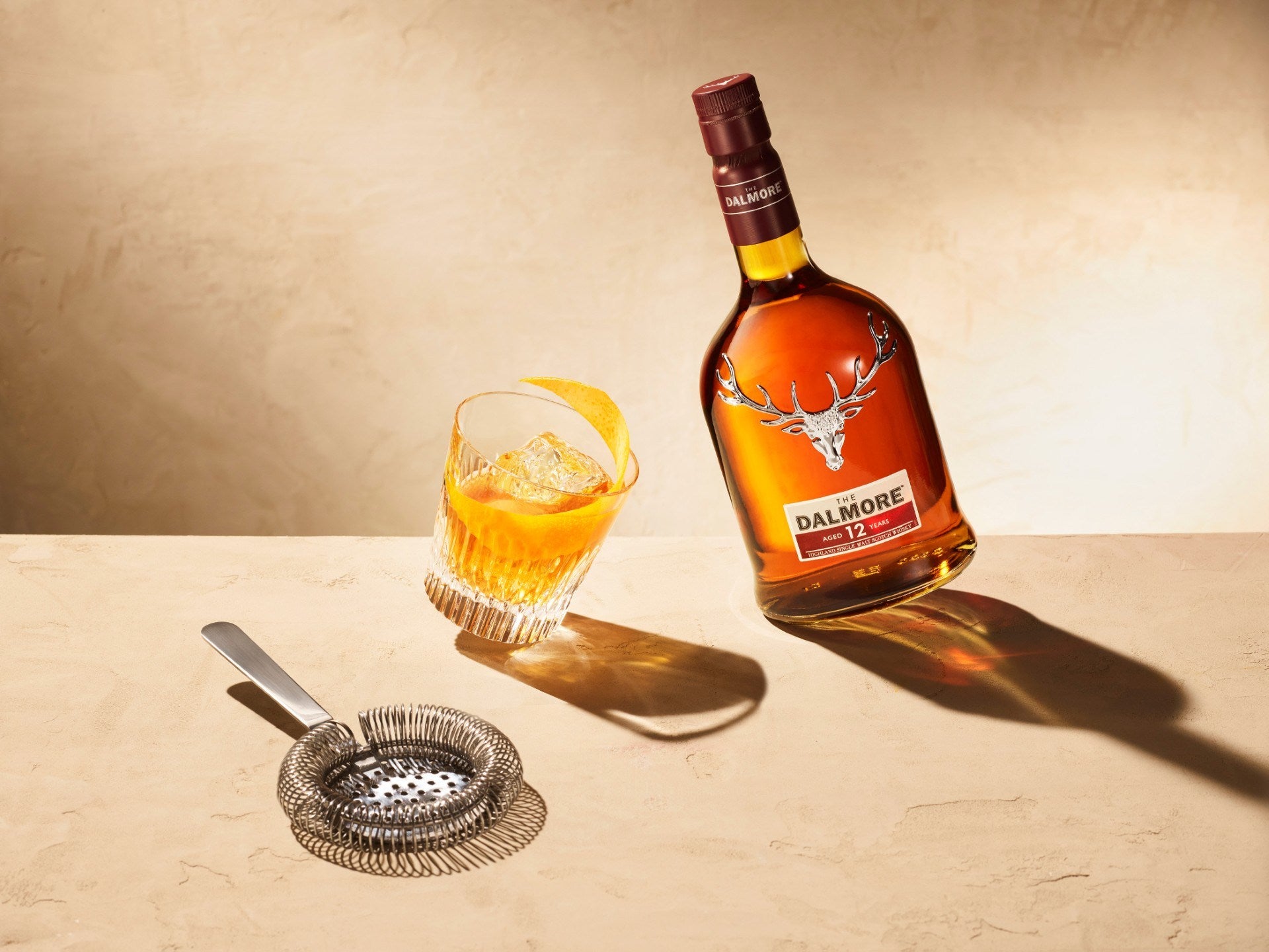 Garrafa de The Dalmore 12 anos ao lado de copo com gelo e twist de laranja